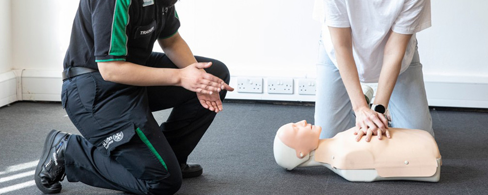 A woman taking instructions from a St John Ambulance trainer about chest compressions.