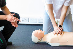 A woman taking instructions from a St John Ambulance trainer about chest compressions.