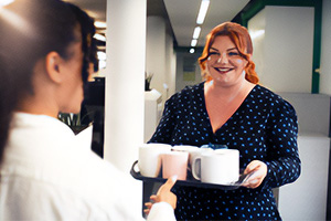A woman carrying a tray with drinks and offering one to her colleague.