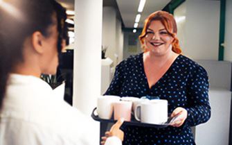 A woman carrying a tray with drinks and offering one to her colleague.