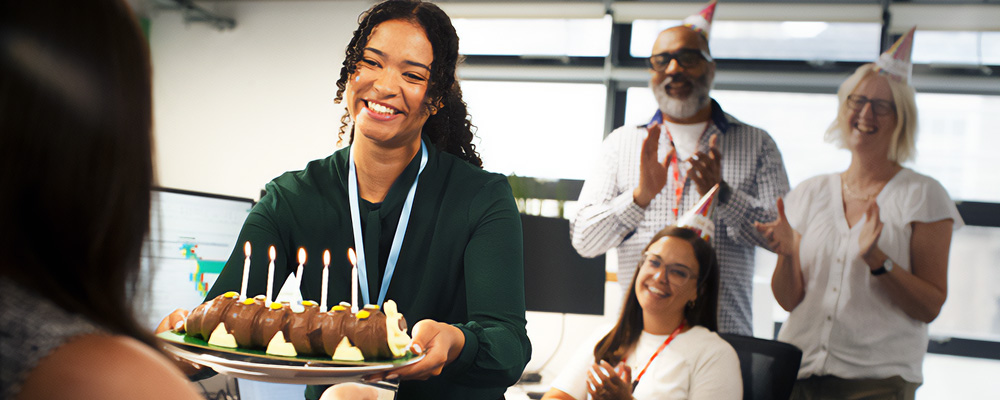 A group of office workers presenting a birthday cake to their colleague.