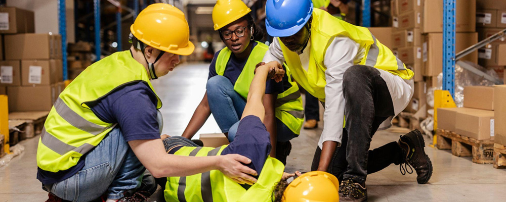 A warehouse worker collapsed on the floor, while his colleagues tend to him.